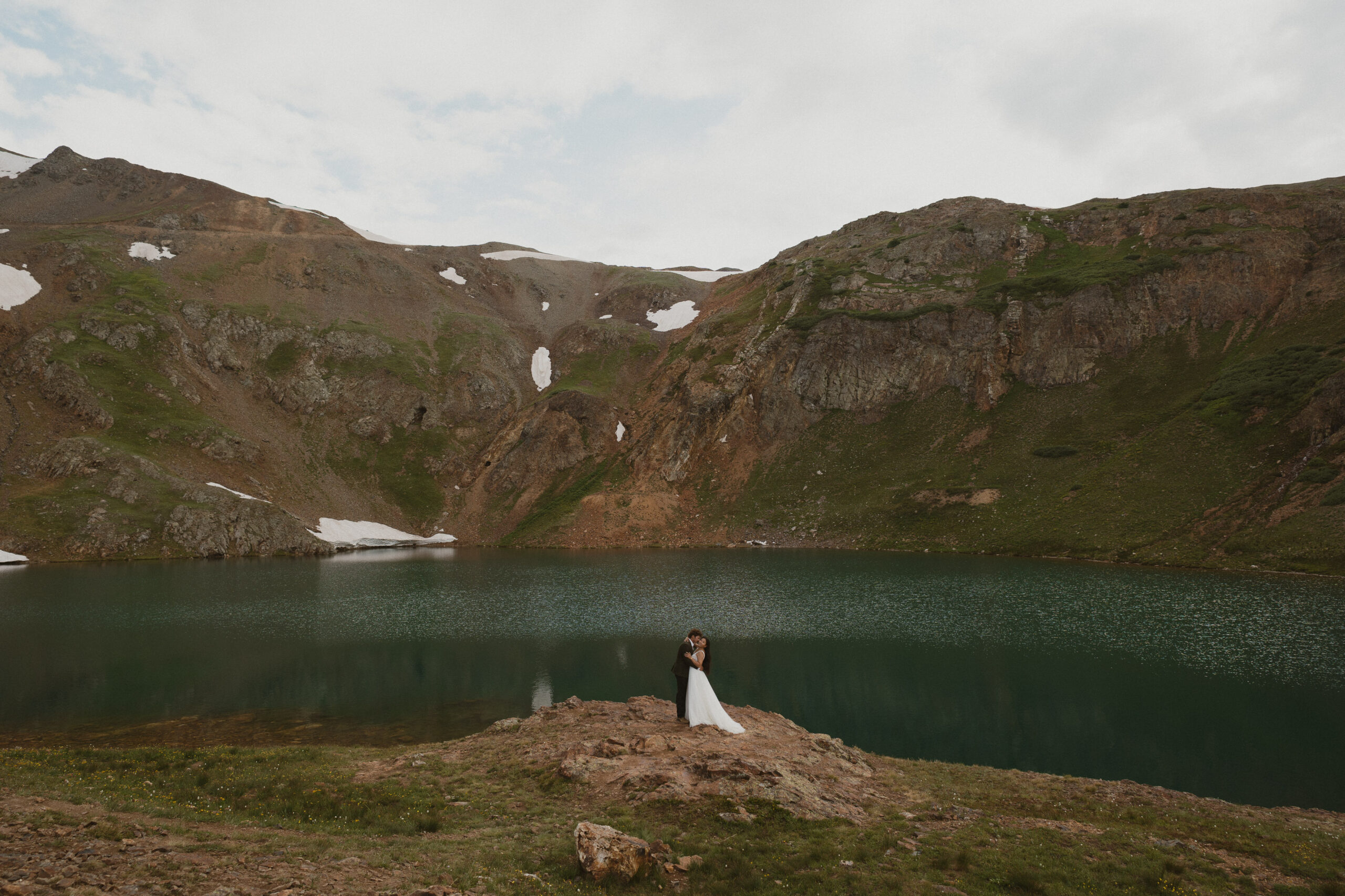 Couple standing by alpine lake on their wedding day