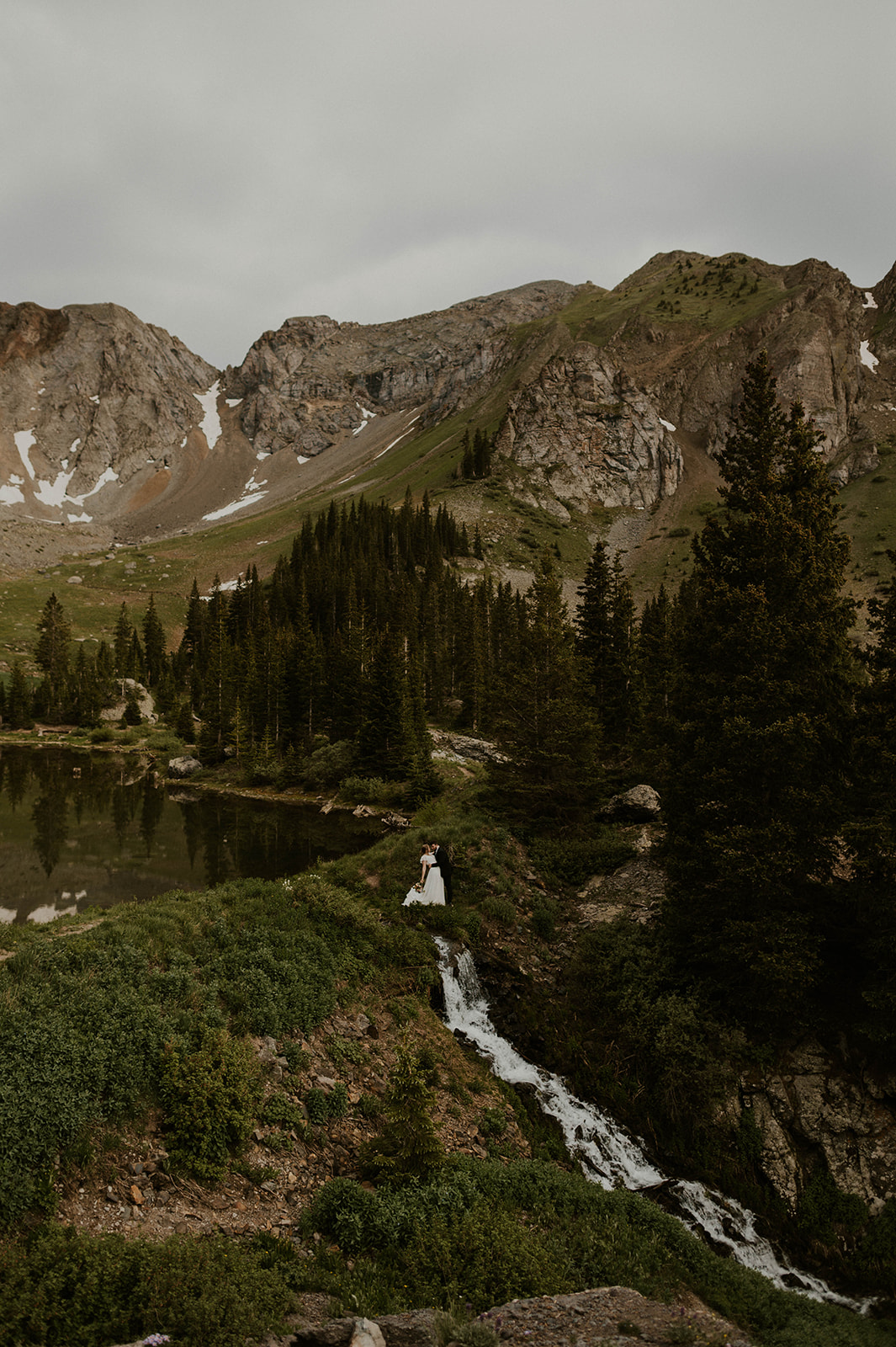 Couple standing next to waterfall and alpine lake in telluride